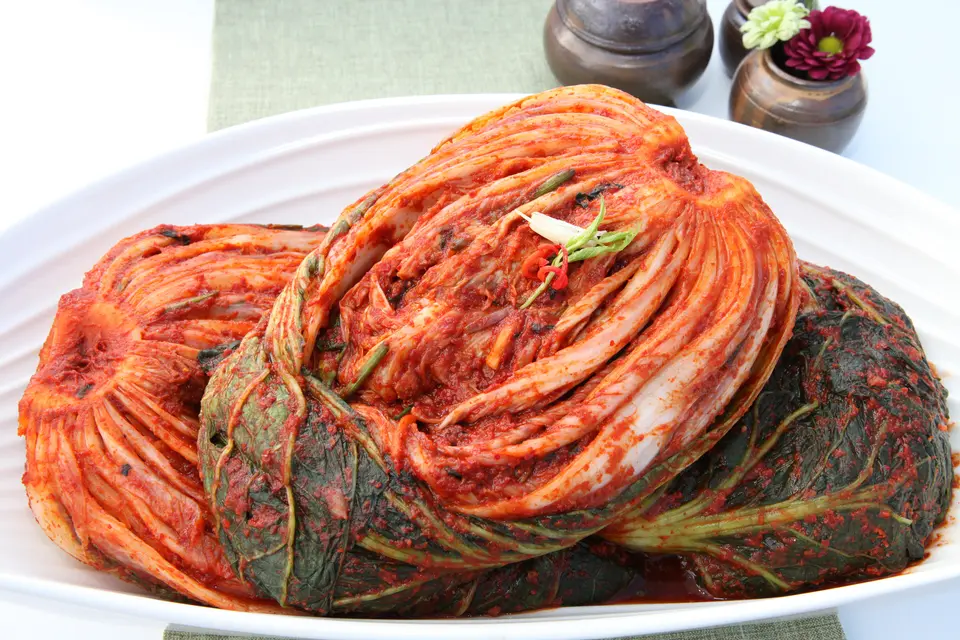 Ein ganzer Kopf Baechu-Kimchi auf weißem Teller, die rote Paste zwischen jedes Blatt gestrichen