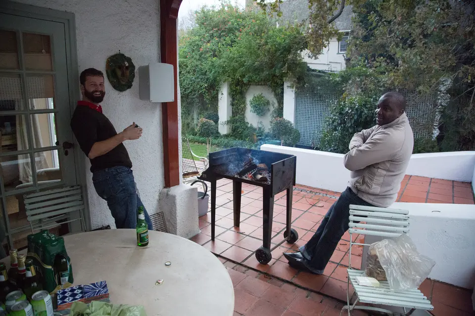 Dos hombres junto a un braai en un porche sudafricano, esperando el fuego