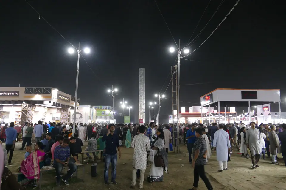 La foule entre les stands éclairés de la Foire du livre d'Ekushey à Dacca, à la nuit tombée