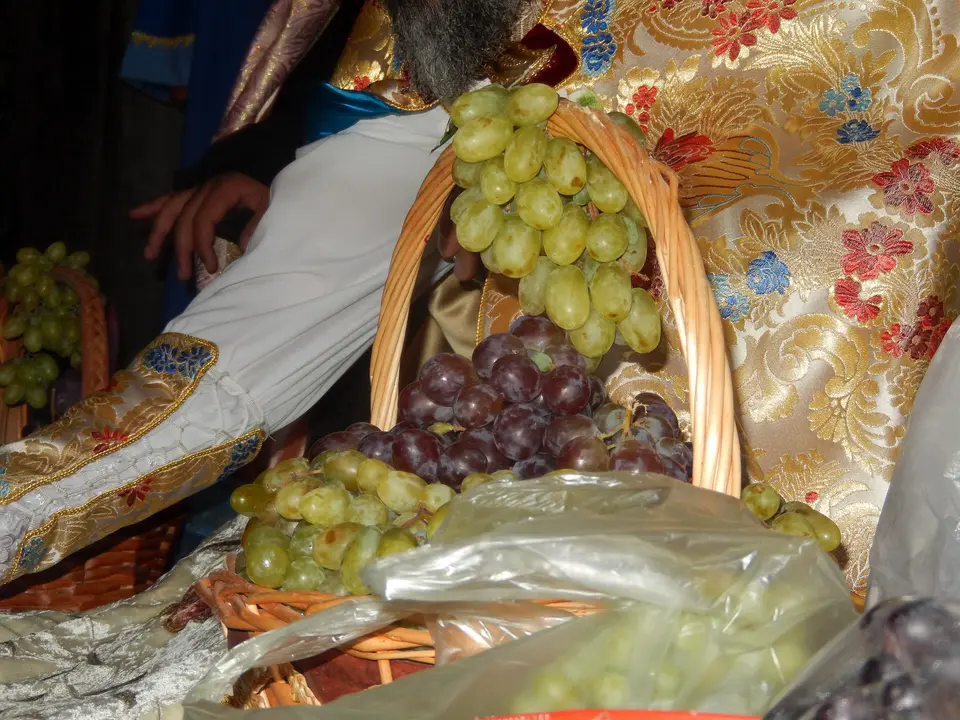 لقطة قريبة لسلال من الخوص مملوءة بالعنب الأخضر والأسود على قماش مطرّز، في انتظار البركة