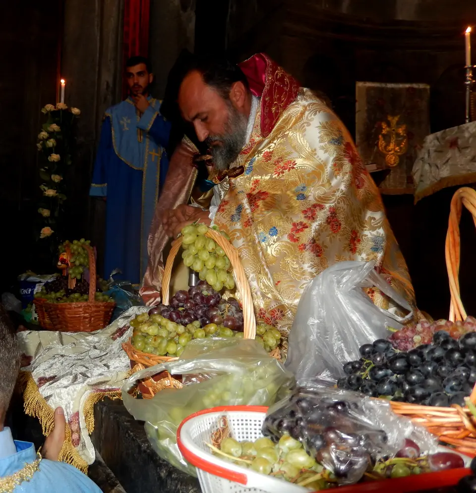 كاهن بثوب ذهبي ينحني على سلال من العنب الأخضر والأسود أثناء بركة العنب في أرمينيا