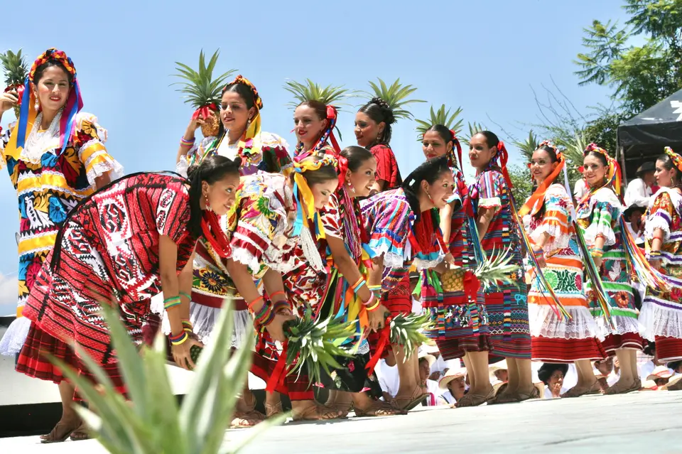 Women in embroidered huipiles holding pineapples in the Flor de Piña dance at the Guelaguetza