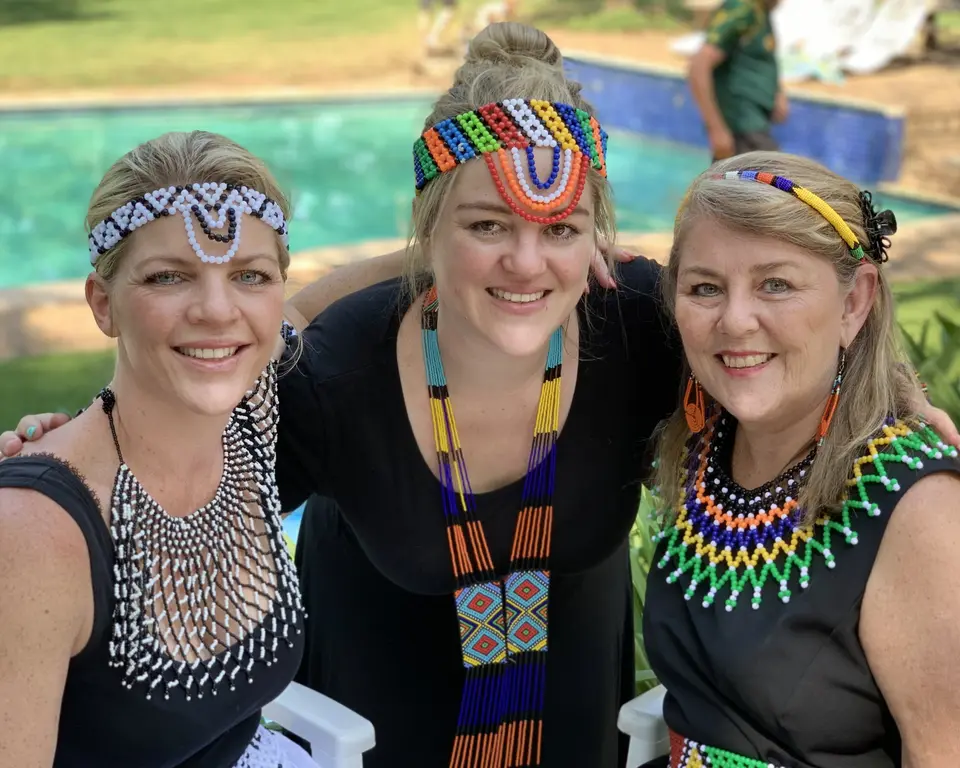 Tres mujeres con cintas y collares de abalorios, celebrando el Heritage Day en Sudáfrica
