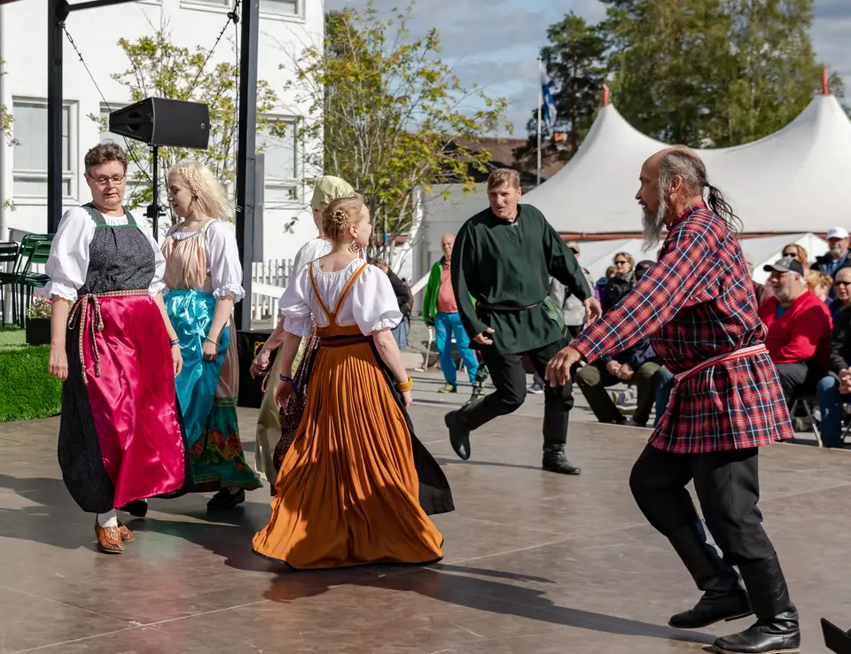 Bailarines con traje popular finlandés girando en un escenario al aire libre en el Festival de Kaustinen