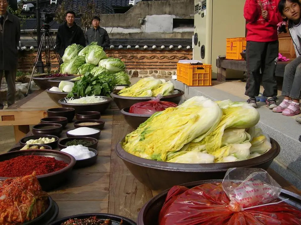 Schalen mit Chilipulver, Knoblauch, Salz und geschnittenem Gemüse neben ganzen Chinakohlköpfen vor einem Kimjang