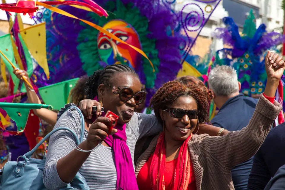 Two women dance in front of feathered costumes at Notting Hill Carnival, 2014