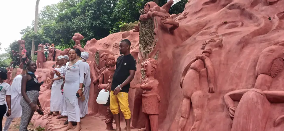 People dressed in white beside the sculpted walls of the Osun Sacred Grove, 2023