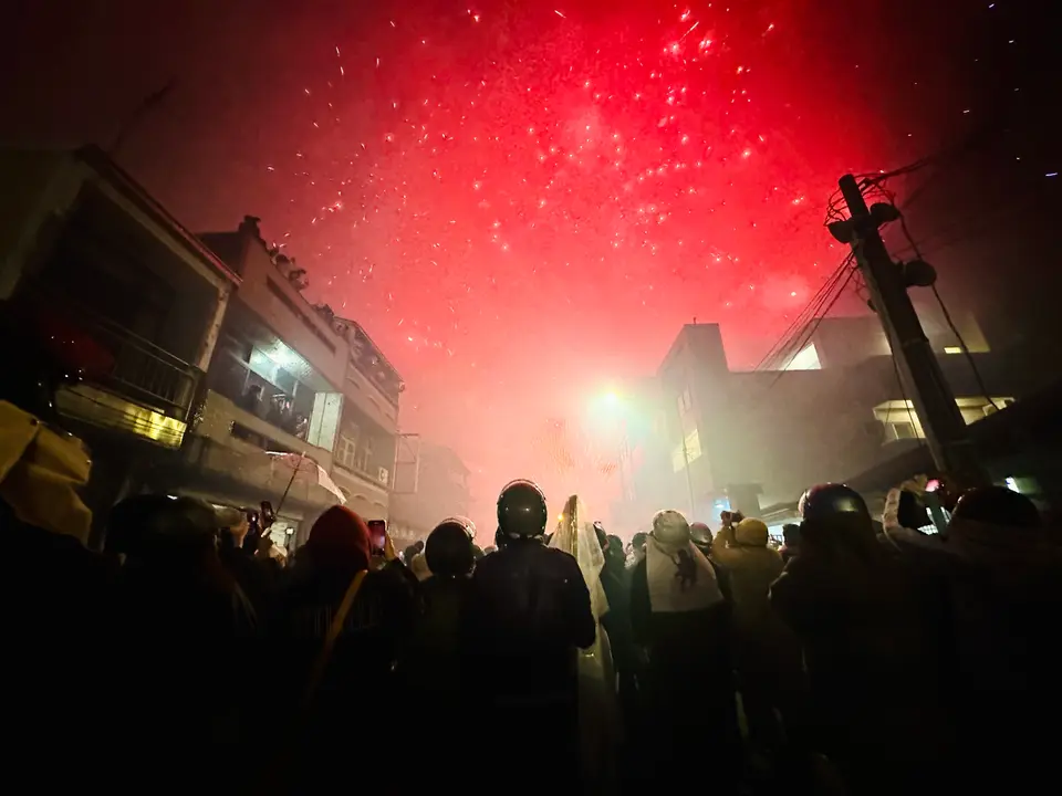 Participants in helmets and protective clothing under a red glow of fireworks in Yanshui, 2023